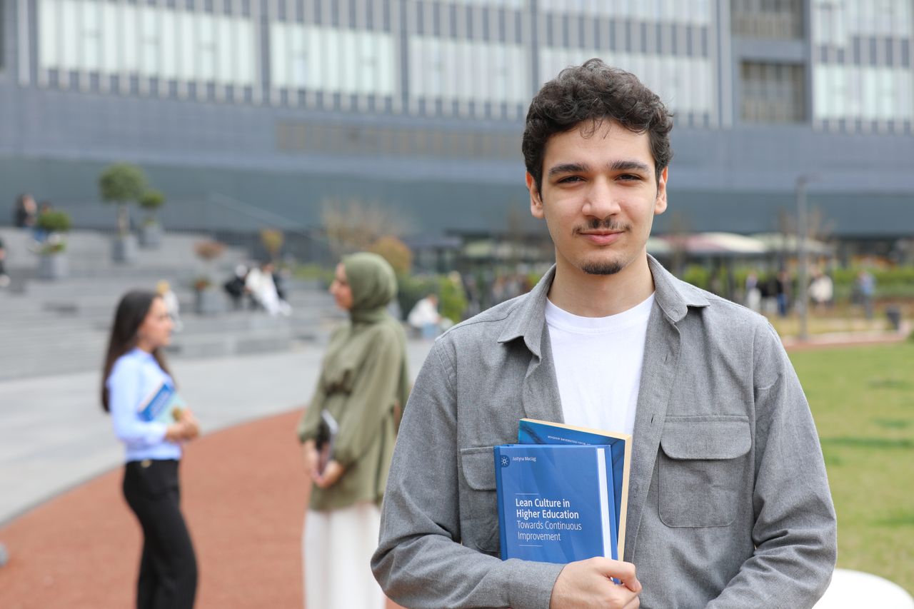 Services A young adult student stands outside on campus holding textbooks, symbolizing education.