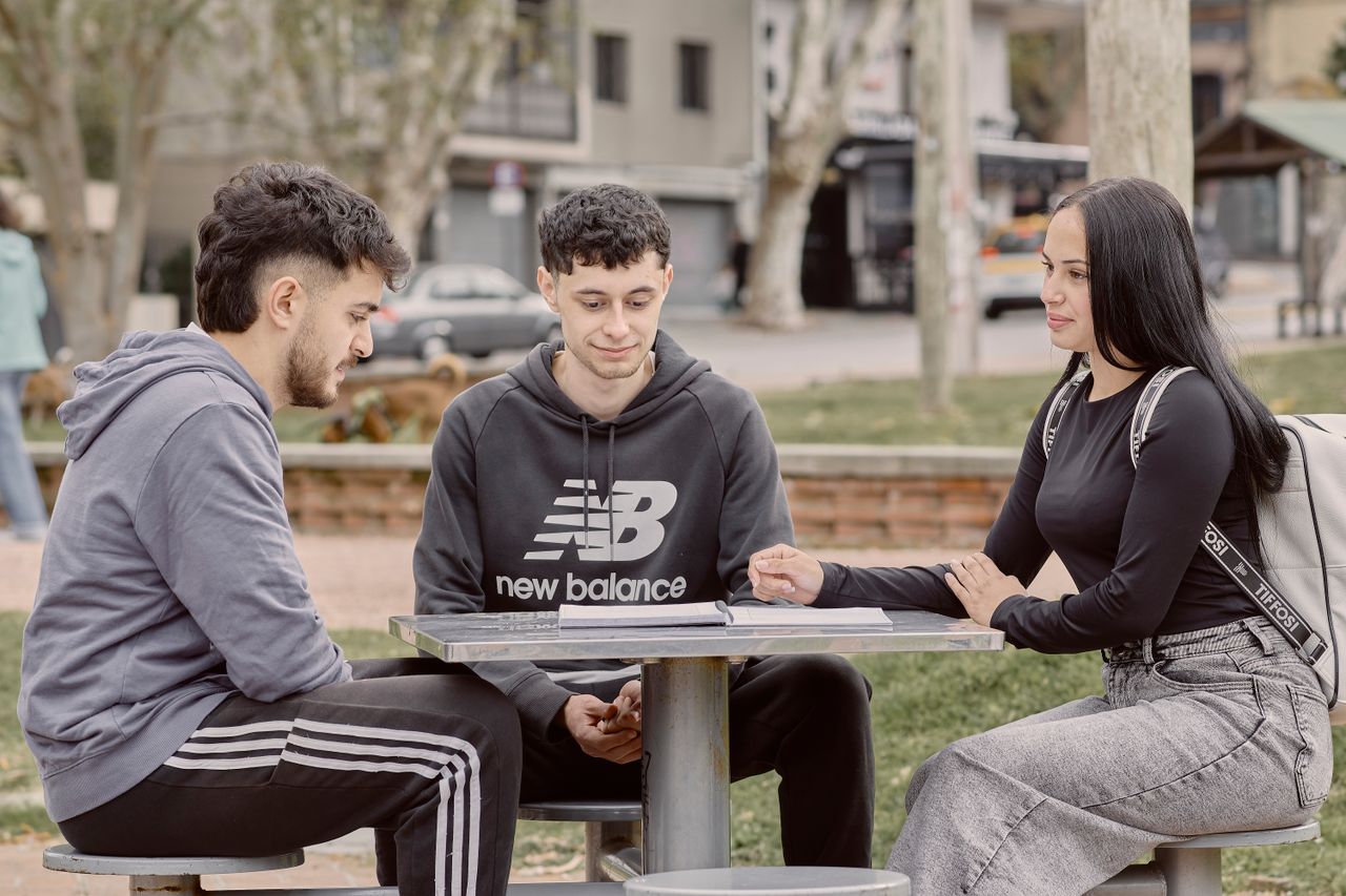 Services Three young adults studying together outdoors at a picnic table in a park setting in Uruguay, capturing social interaction and collaboration.