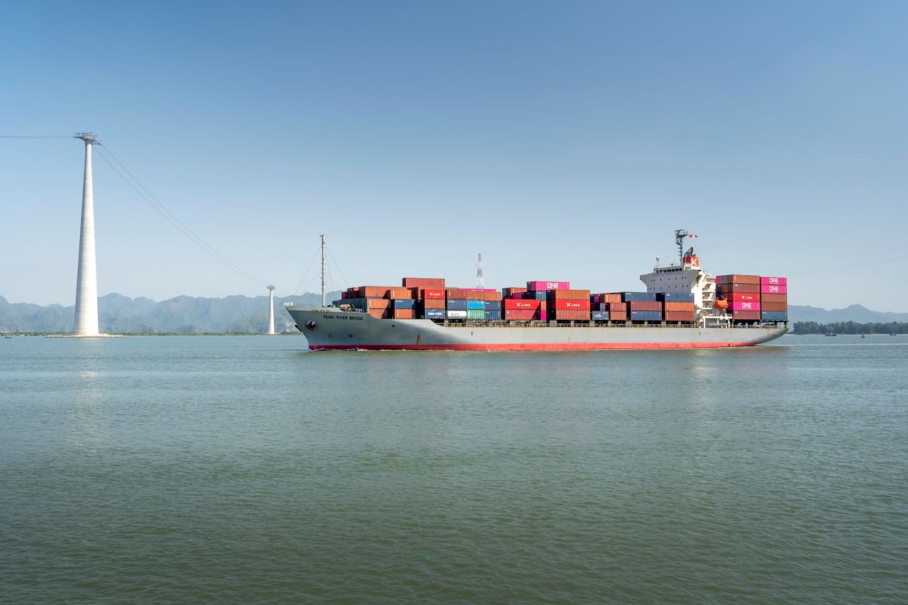 Services A large cargo ship carrying colorful containers sails smoothly across a calm ocean on a clear sunny day.